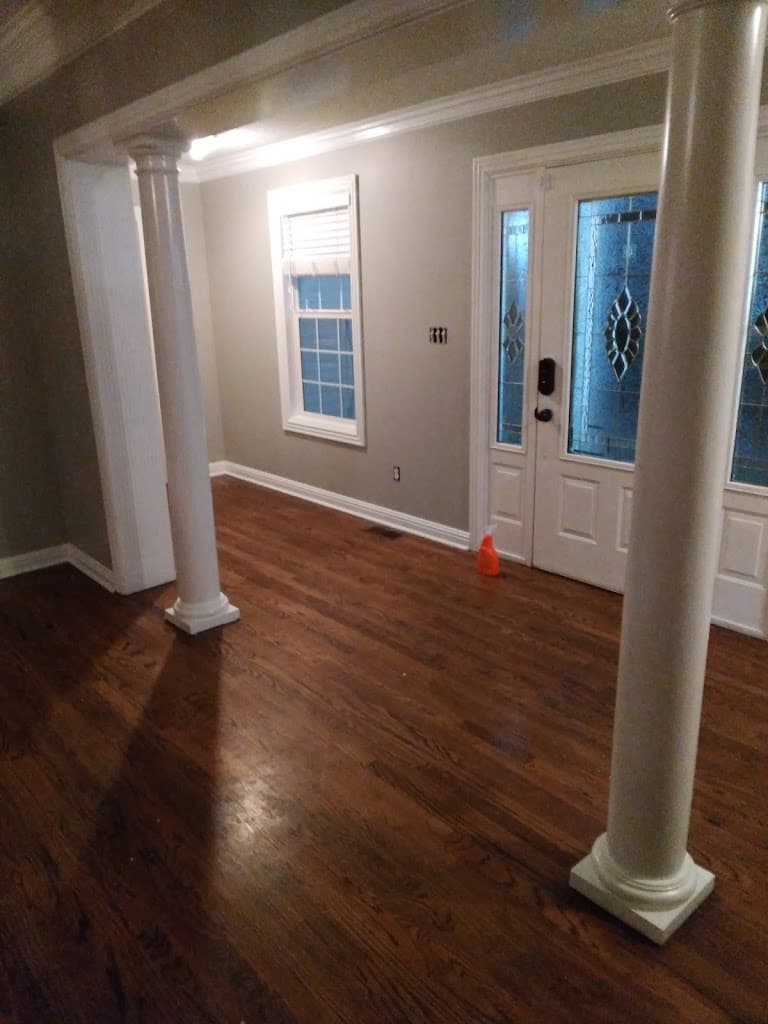 Finished living room with columns, hardwood floor, and stained-glass front door